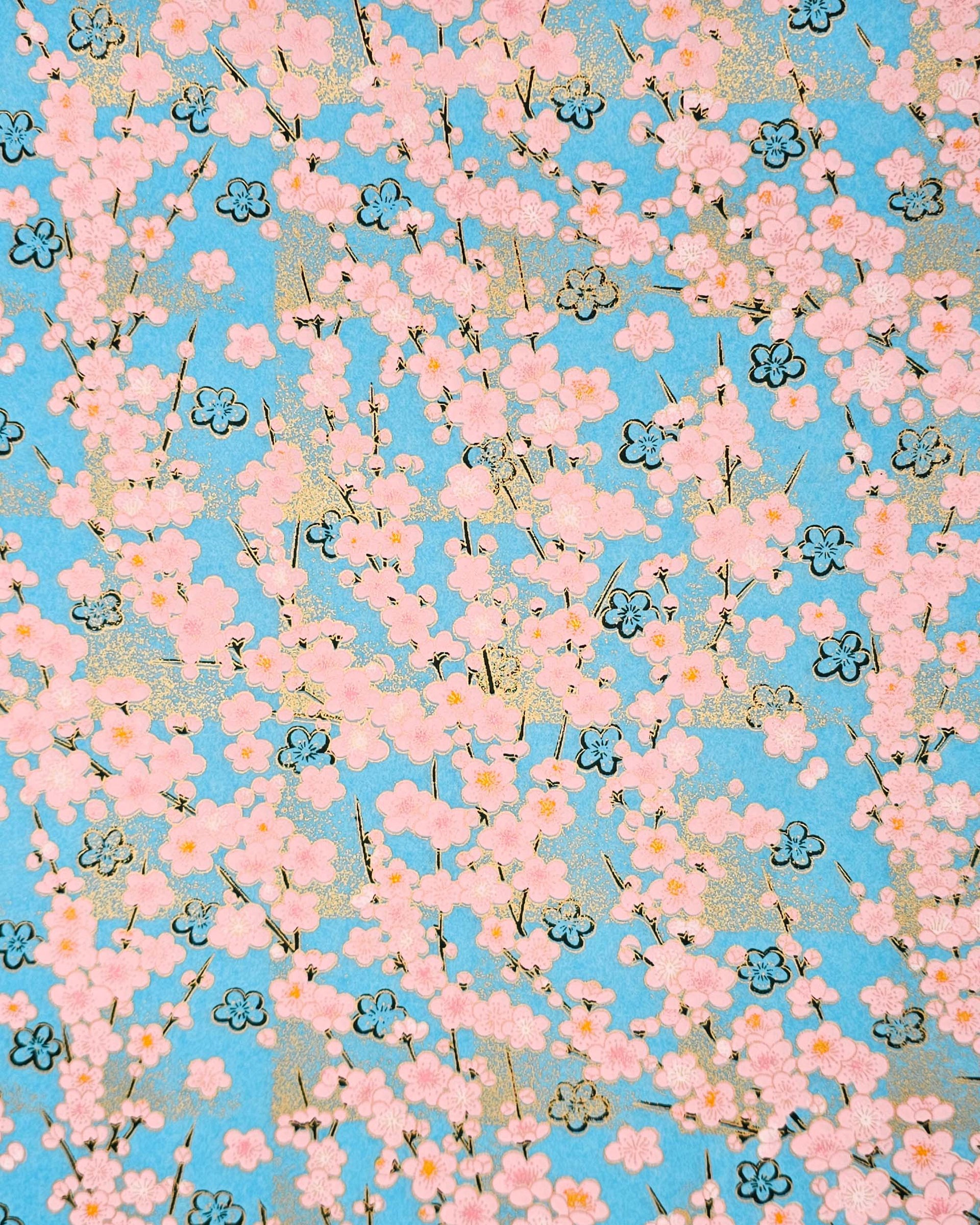 Japanese chiyogami featuring pink plum blossoms and black plum blossom outines on a light blue background with metallic gold accents.