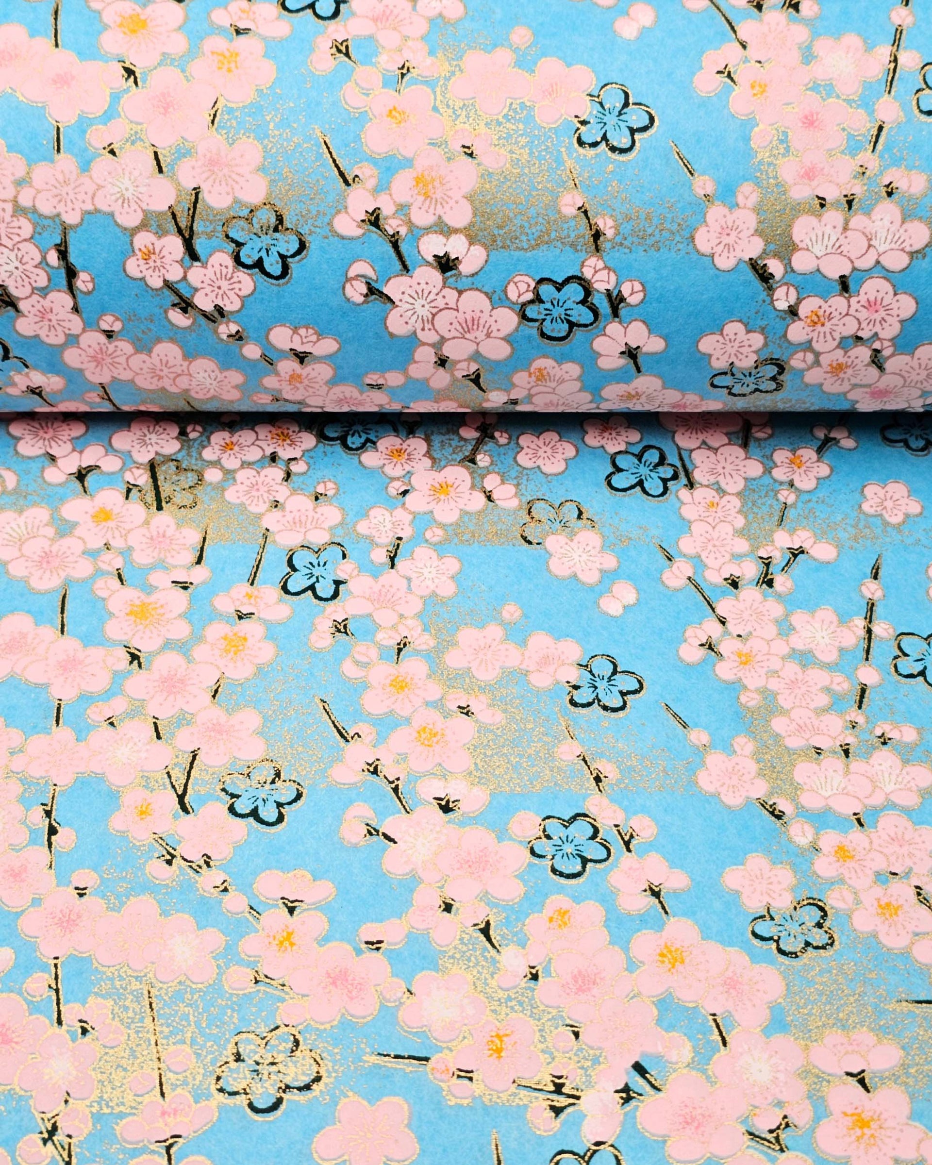 Japanese chiyogami featuring pink plum blossoms and black plum blossom outines on a light blue background with metallic gold accents.