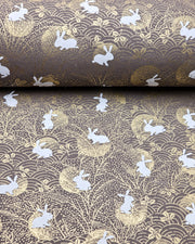 Japanese chiyogami paper featuring white rabbits with gold moons on a brown background with metallic gold accents.