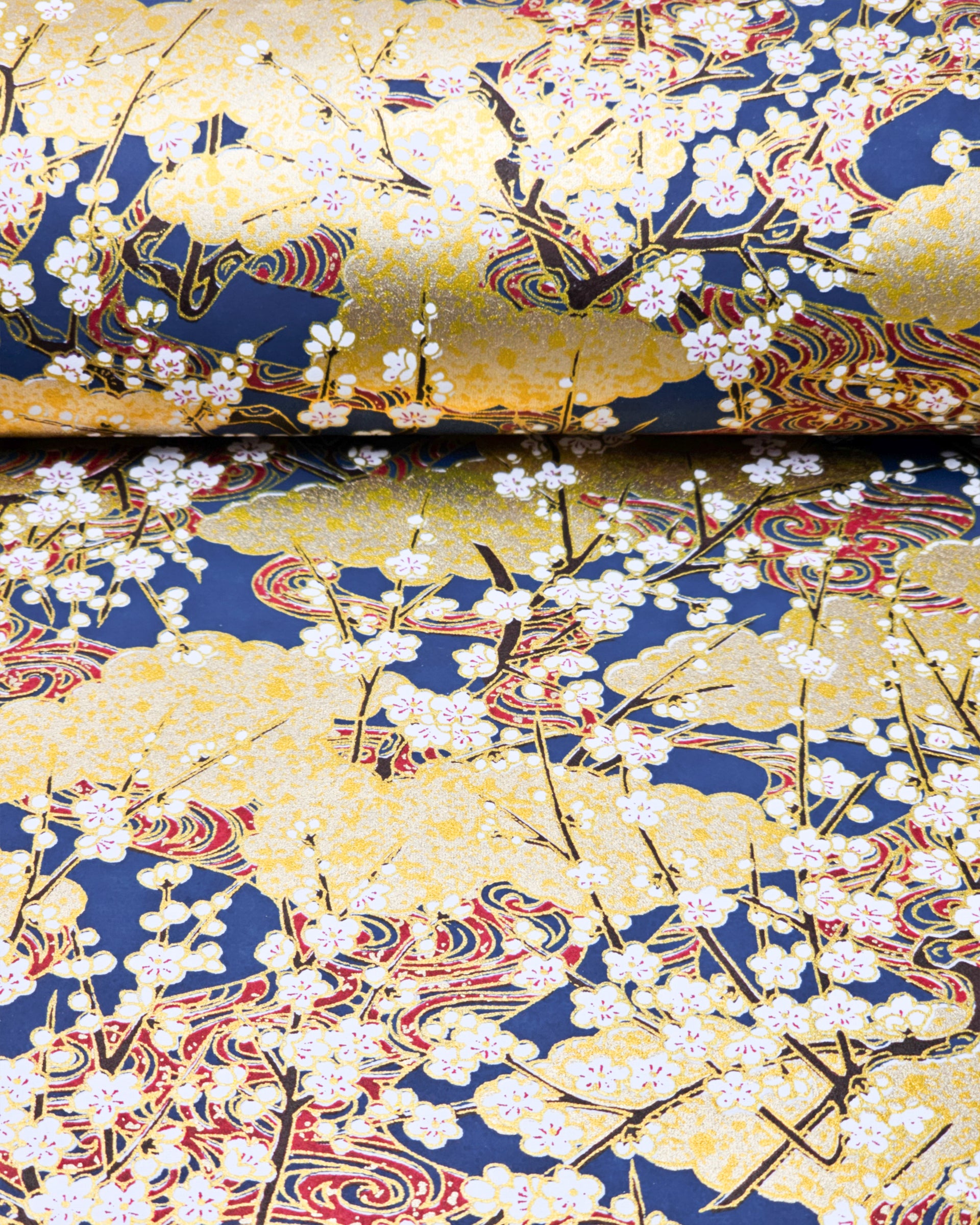 Japanese chiyogami paper featuring white plum blossom branches with red swirls on a blue and gold background with metallic gold accents.