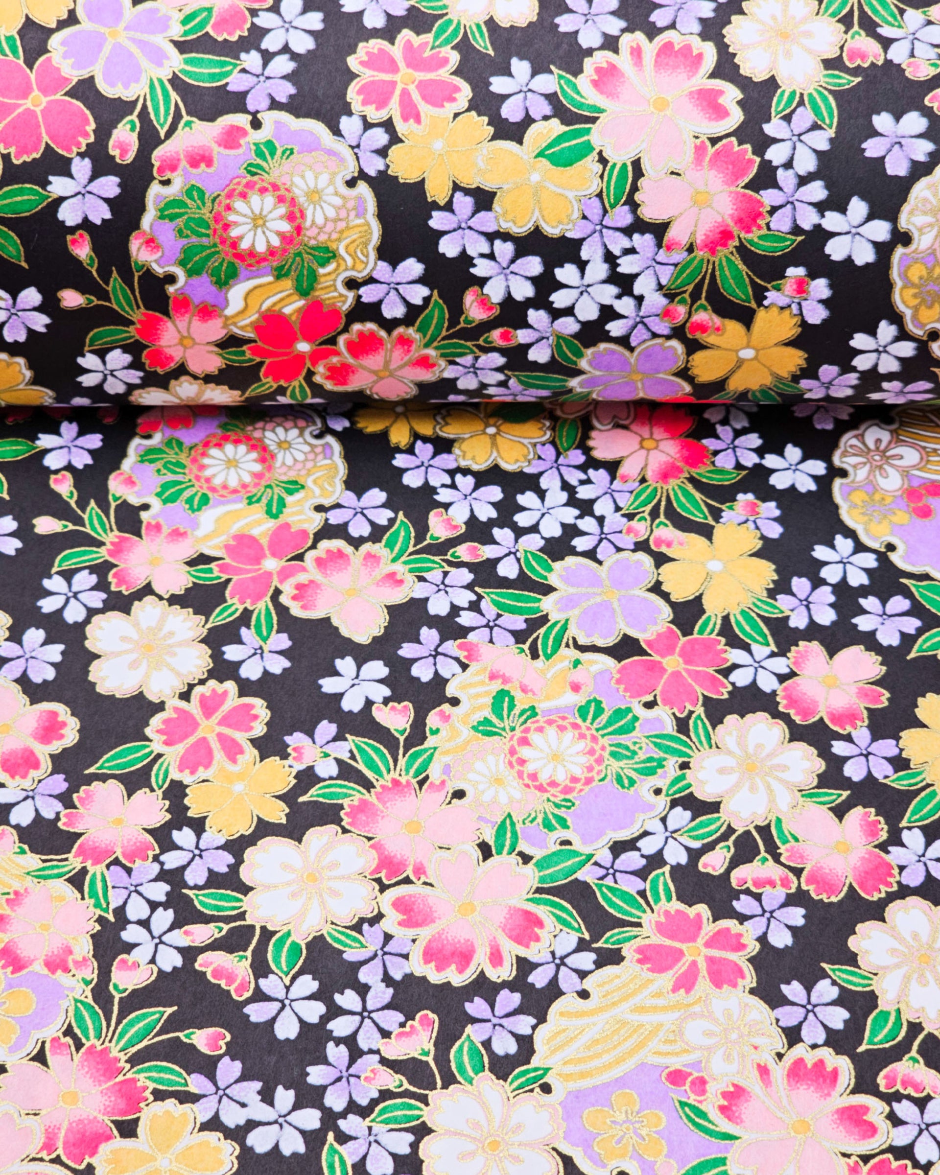 Japanese chiyogami paper featuring pink, yellow, purple, and white cherry blossoms and purple yukiwas on a black background with metallic gold accents.