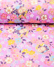 Japanese chiyogami paper featuring pink, yellow, blue, and white cherry blossoms and purple yukiwas on a purple background with metallic gold accents.