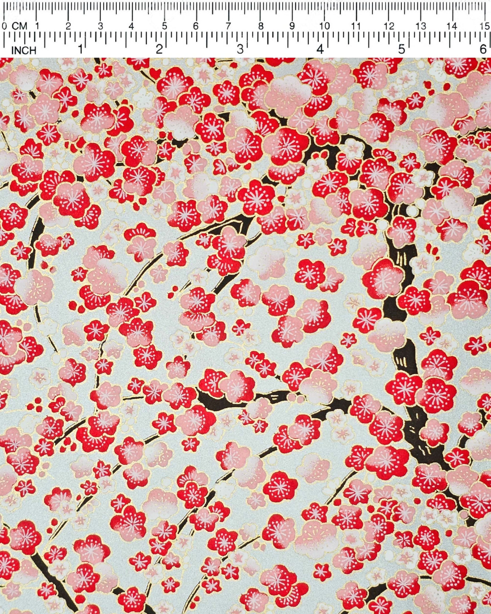 Japanese chiyogami paper featuring a red plum blossom tree with a dark brown tree trunk on a metallic silver background with metallic gold accents.