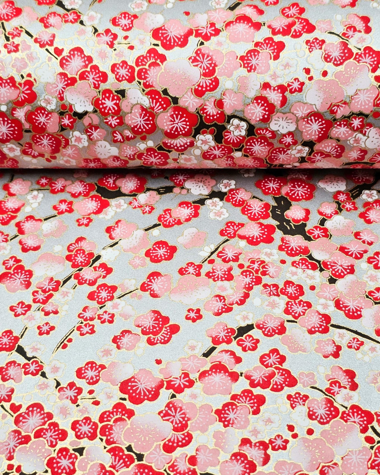 Japanese chiyogami paper featuring a red plum blossom tree with a dark brown tree trunk on a metallic silver background with metallic gold accents.