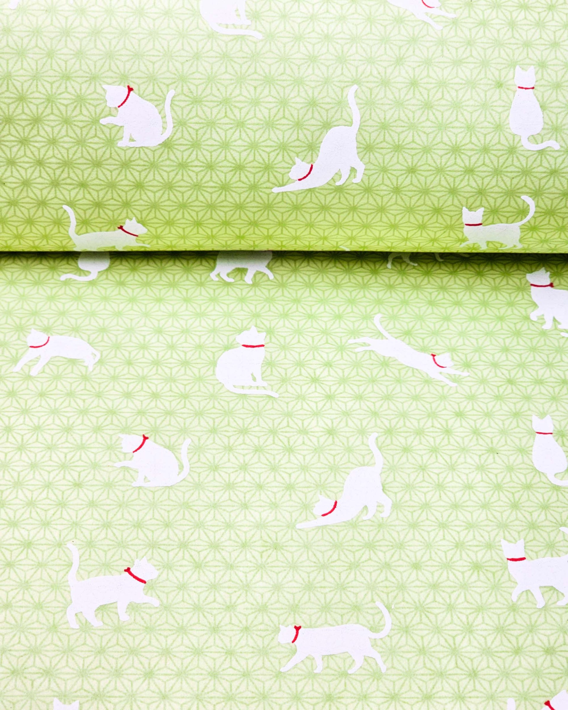 Japanese chiyogami featuring white cats with red collars on a green asanoha (hemp leaf) background.