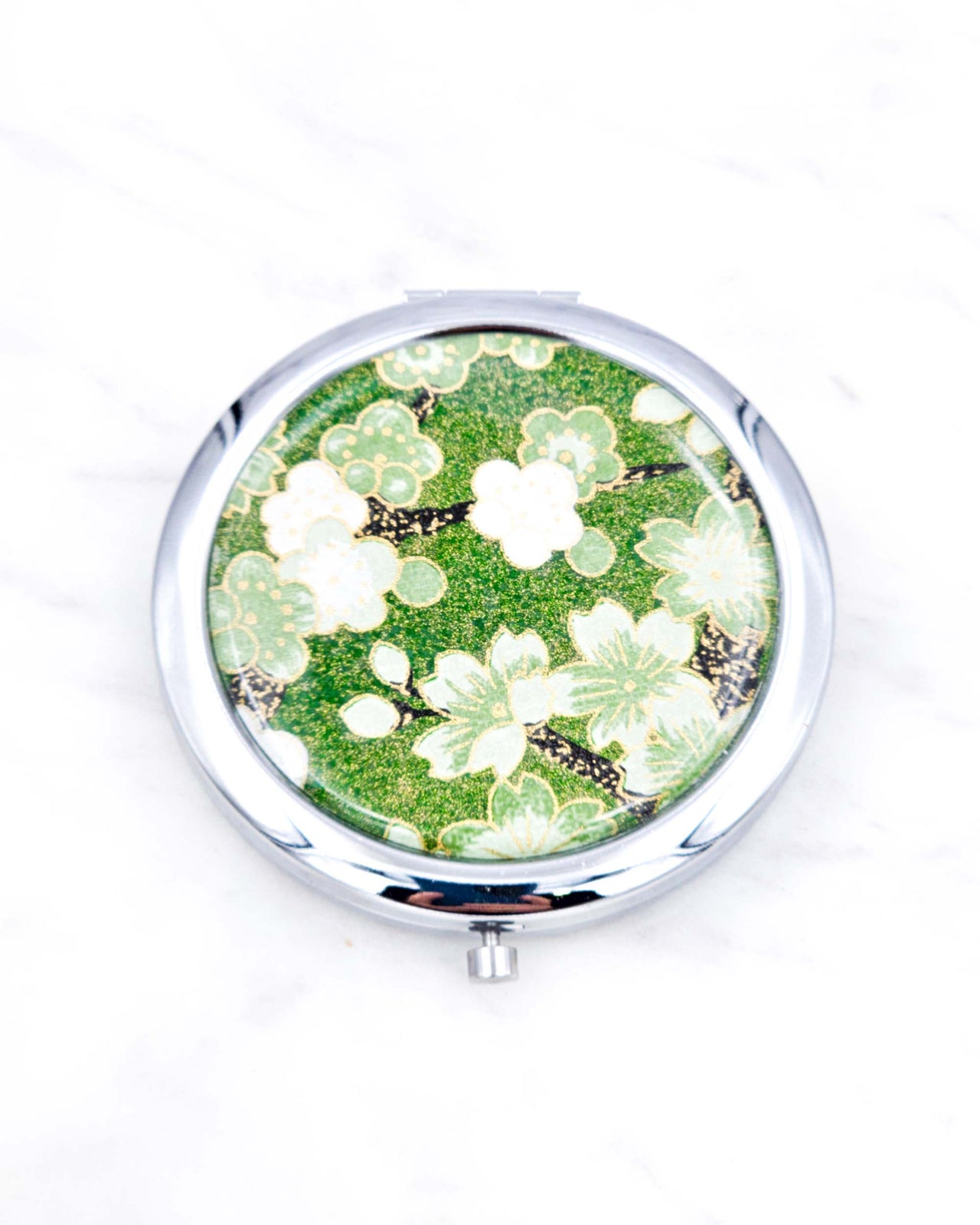 Silver metal compact mirror featuring green cherry blossoms on a green background with metallic gold accents.