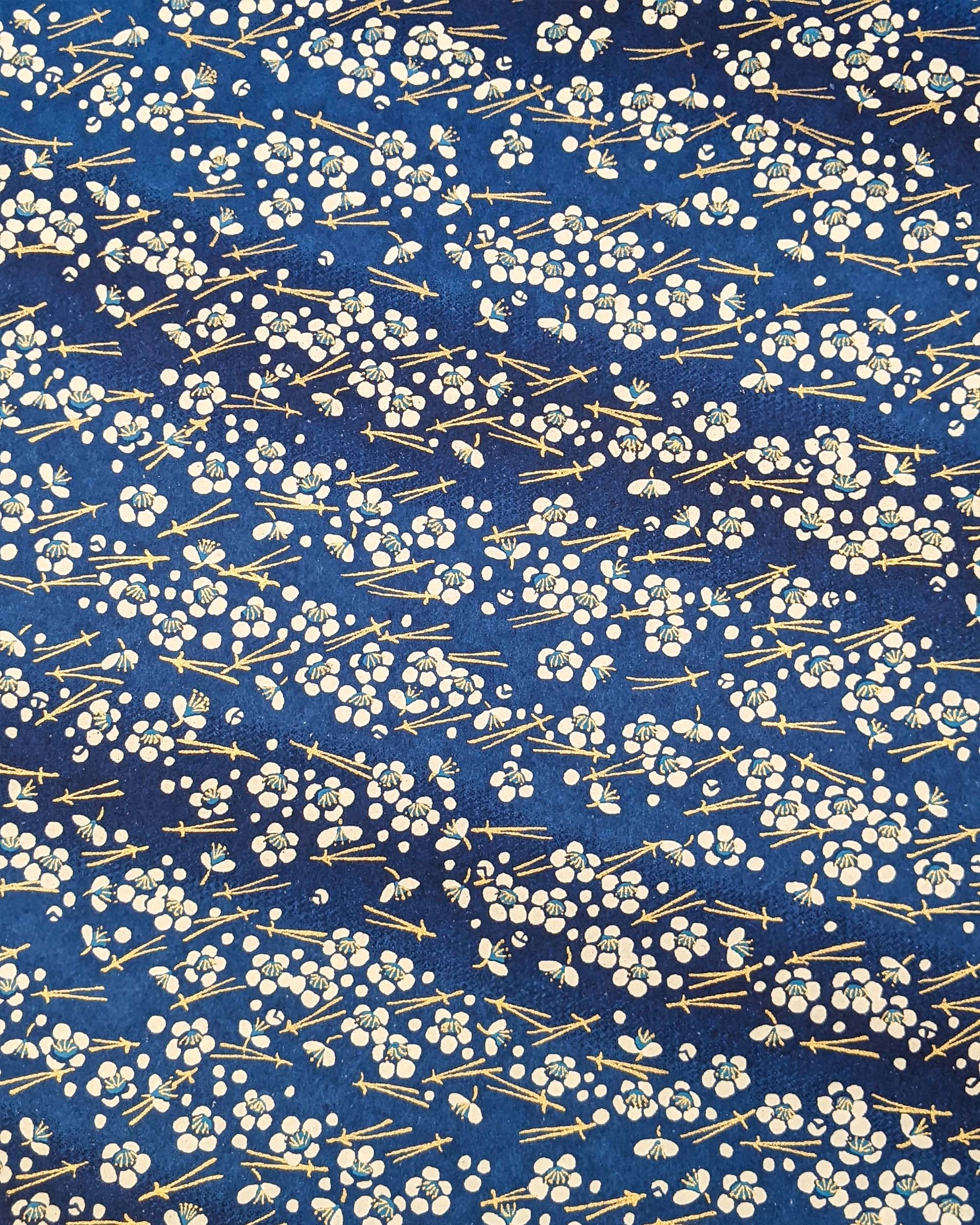 Japanese chiyogami featuring small white plum blossoms & matsuba (pine needles) on a blue background with metallic gold accents.
