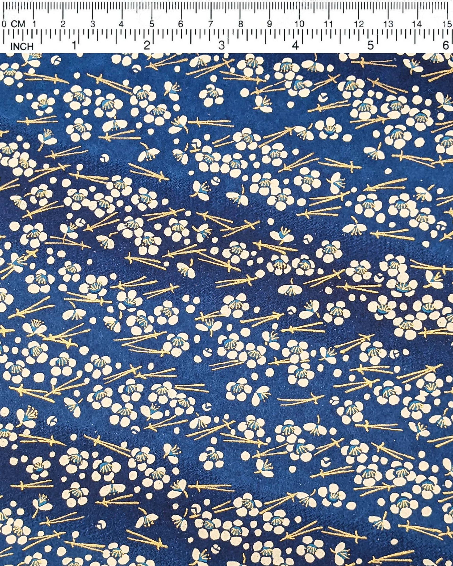 Japanese chiyogami featuring small white plum blossoms & matsuba (pine needles) on a blue background with metallic gold accents.