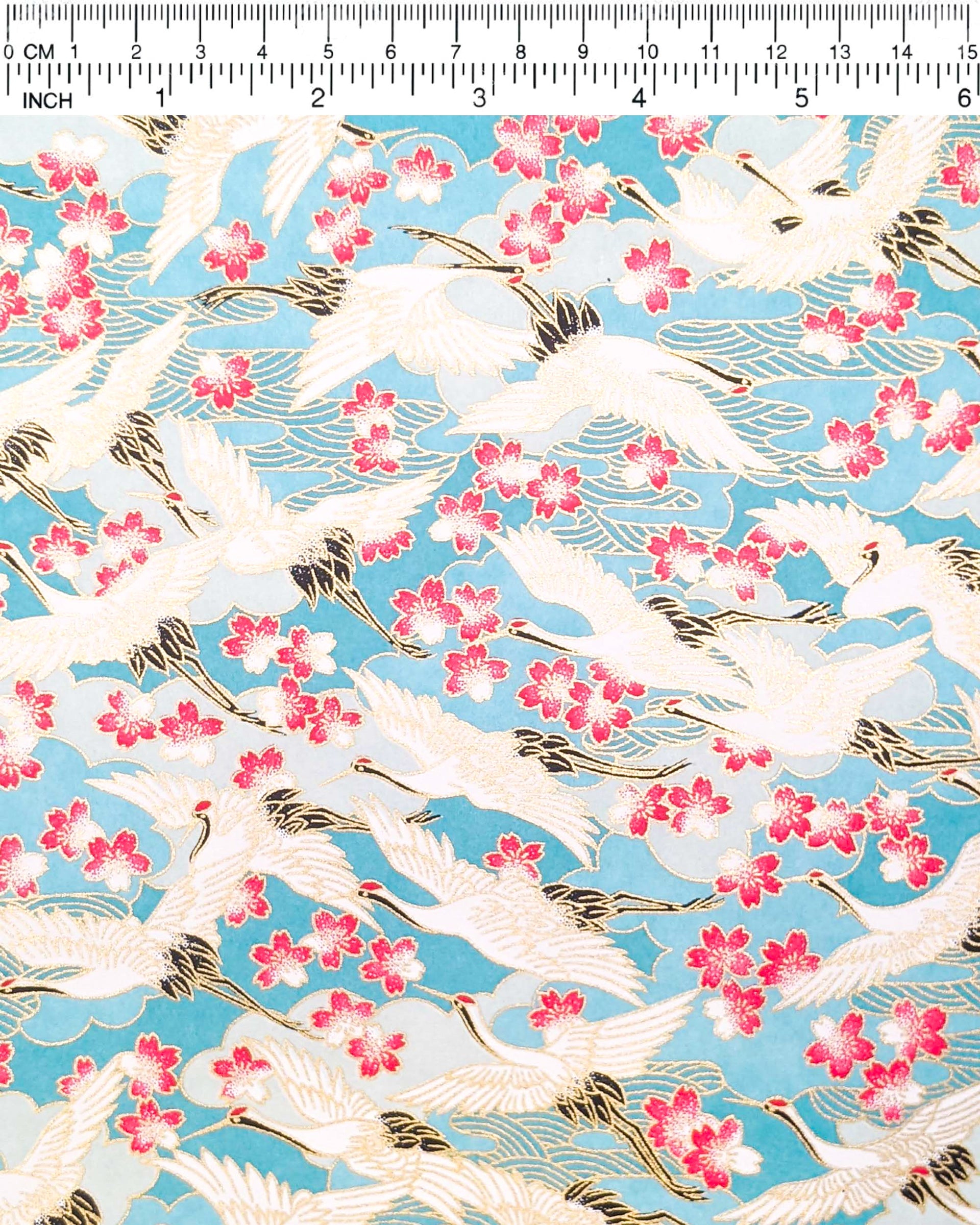 Japanese chiyogami paper featuring flying white cranes and pink cherry blossoms a light blue background with metallic gold accents.