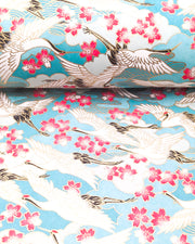 Japanese chiyogami paper featuring flying white cranes and pink cherry blossoms a light blue background with metallic gold accents.