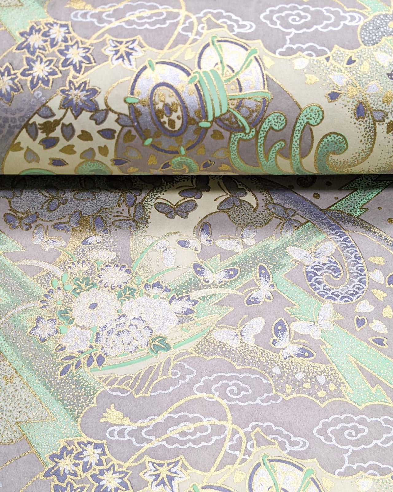 Japanese chiyogami paper featuring a light gray and turquoise stormy seascape with lightning, butterflies, and floral boats with metallic gold and silver accents.