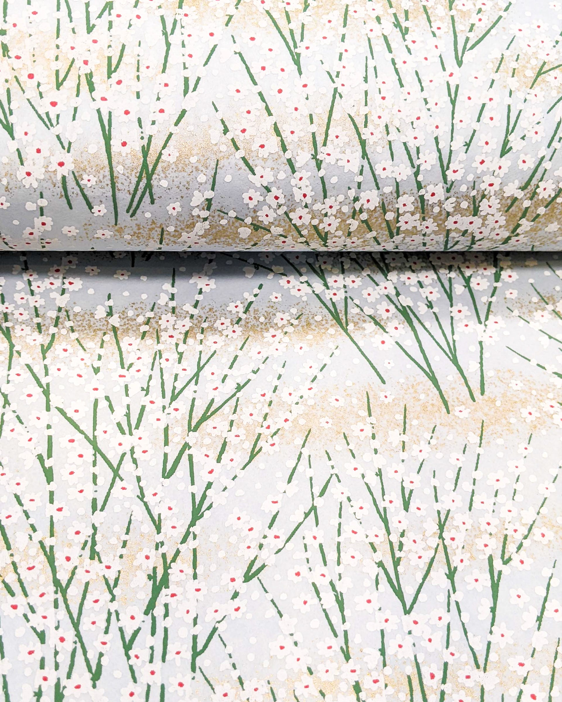Japanese chiyogami paper featuring small white flower bushes over a light blue background with metallic gold accents.