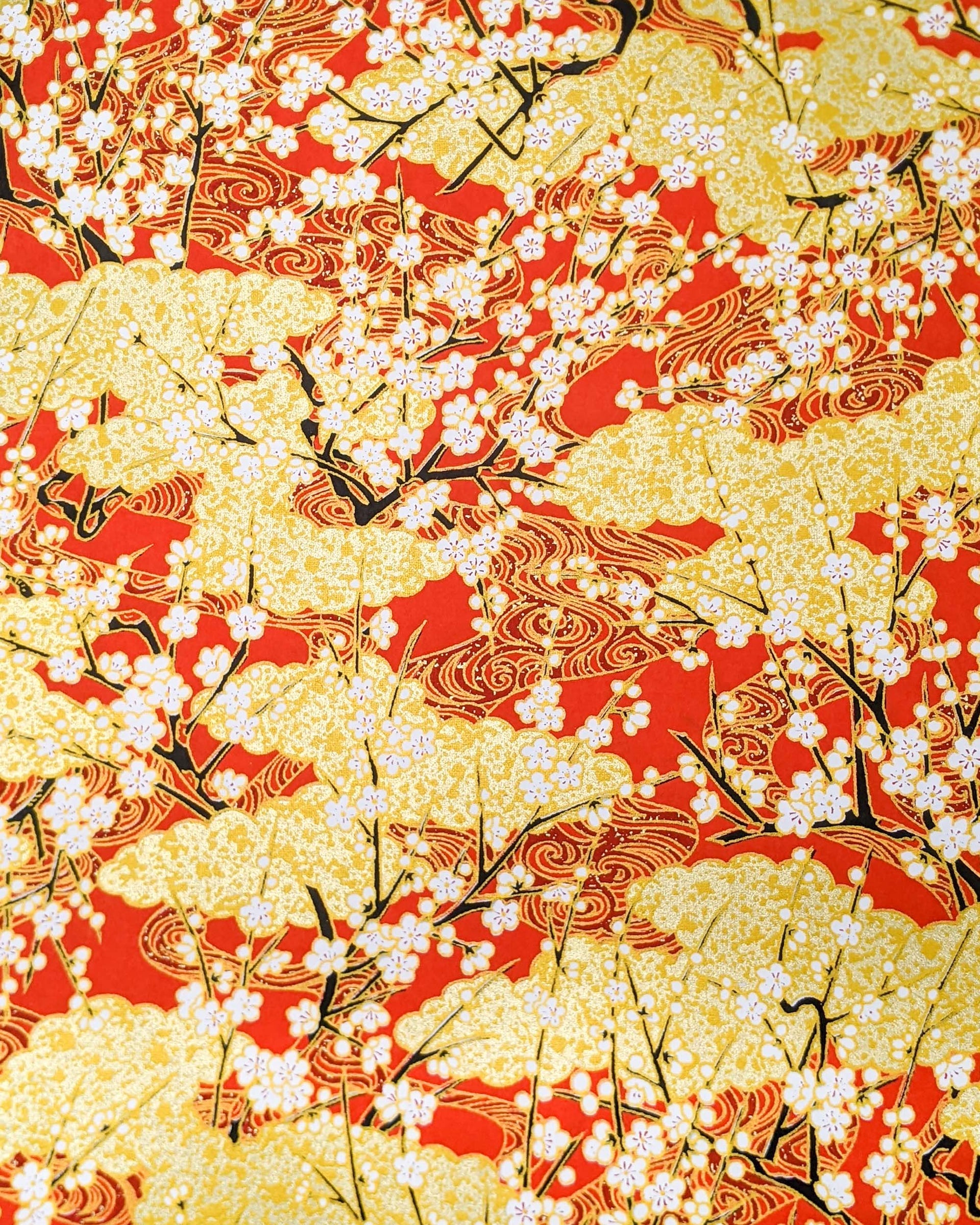 Japanese chiyogami featuring white plum blossom branches on a red and gold background with metallic gold accents.