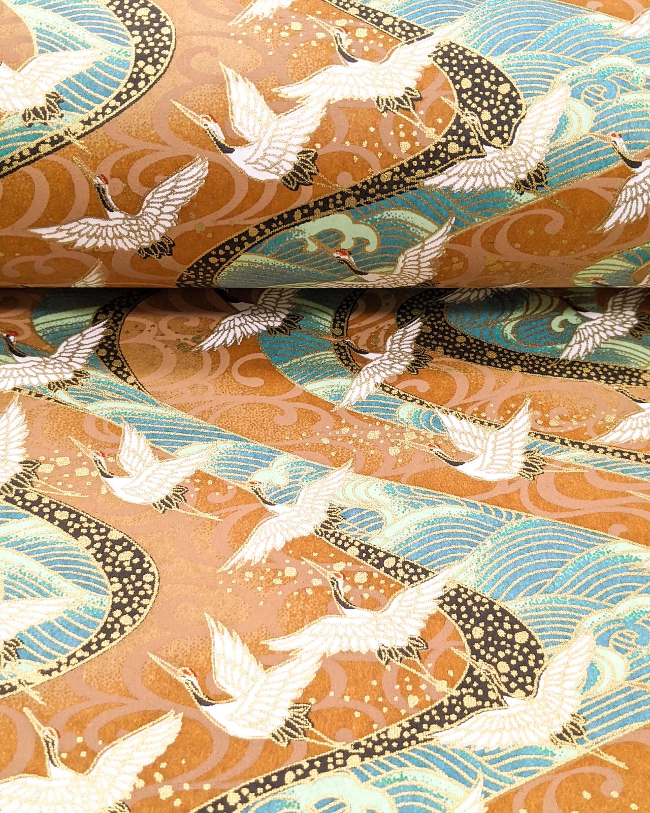 Japanese chiyogami paper featuring cranes flying over turquoise colored rivers on a brown background with metallic gold accents.