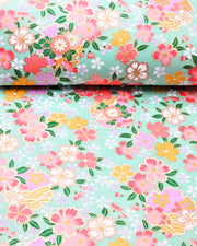 Japanese chiyogami paper featuring pink, yellow, purple, and white cherry blossoms and purple yukiwas on a turquoise background with metallic gold accents.