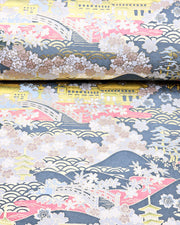 Japanese chiyogami paper featuring a village scene with yellow pagodas, buildings, and bridges with pink water, light gray cherry blossoms on a blue gray background with metallic gold accents