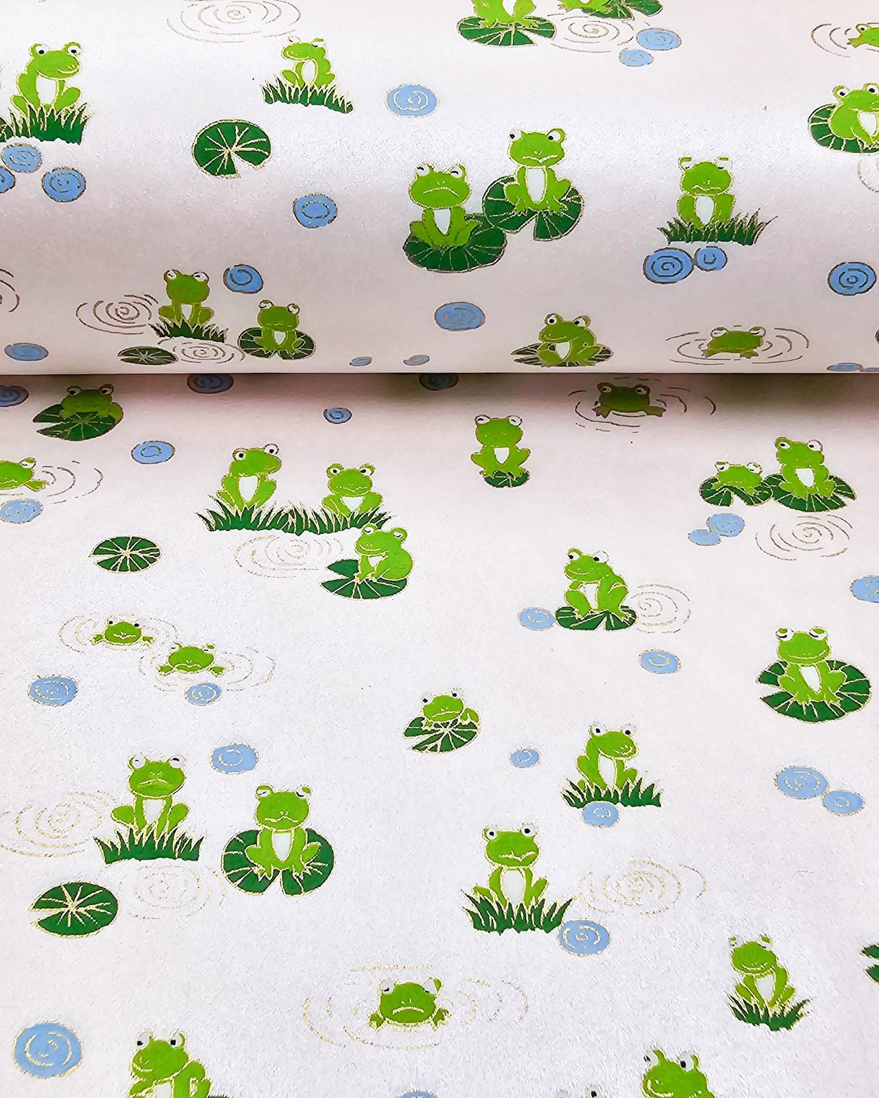Japanese chiyogami featuring green frogs sitting on green lily pads on a pearlescent pink background with metallic gold accents.