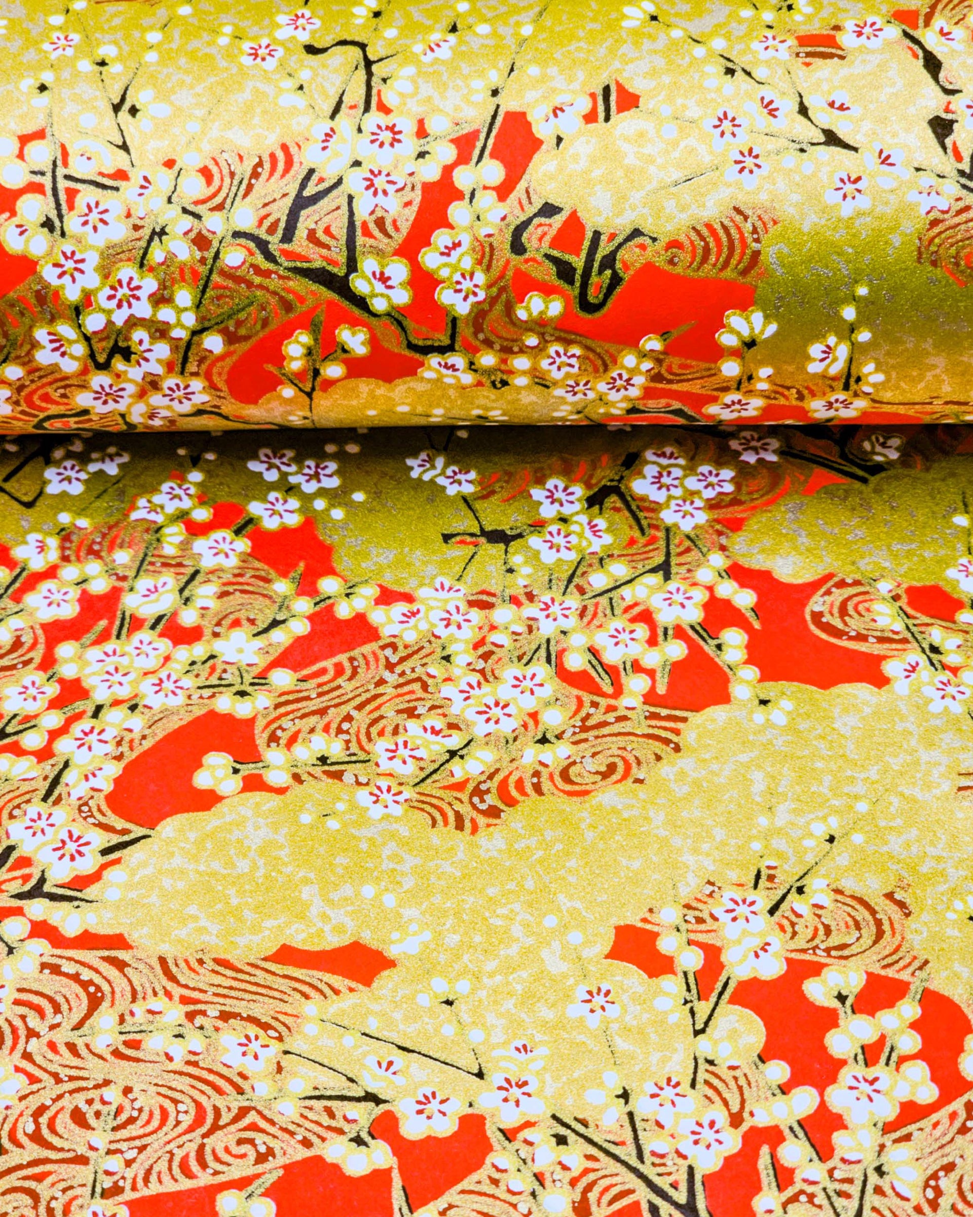 Japanese chiyogami featuring white plum blossom branches on a red and gold background with metallic gold accents.