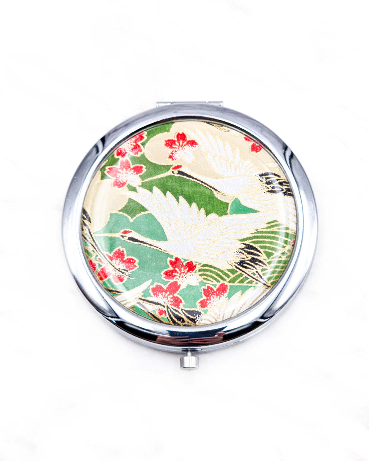 Round silver metal compact mirror featuring white flying cranes and red and white cherry blossoms on a green background with metallic gold details.