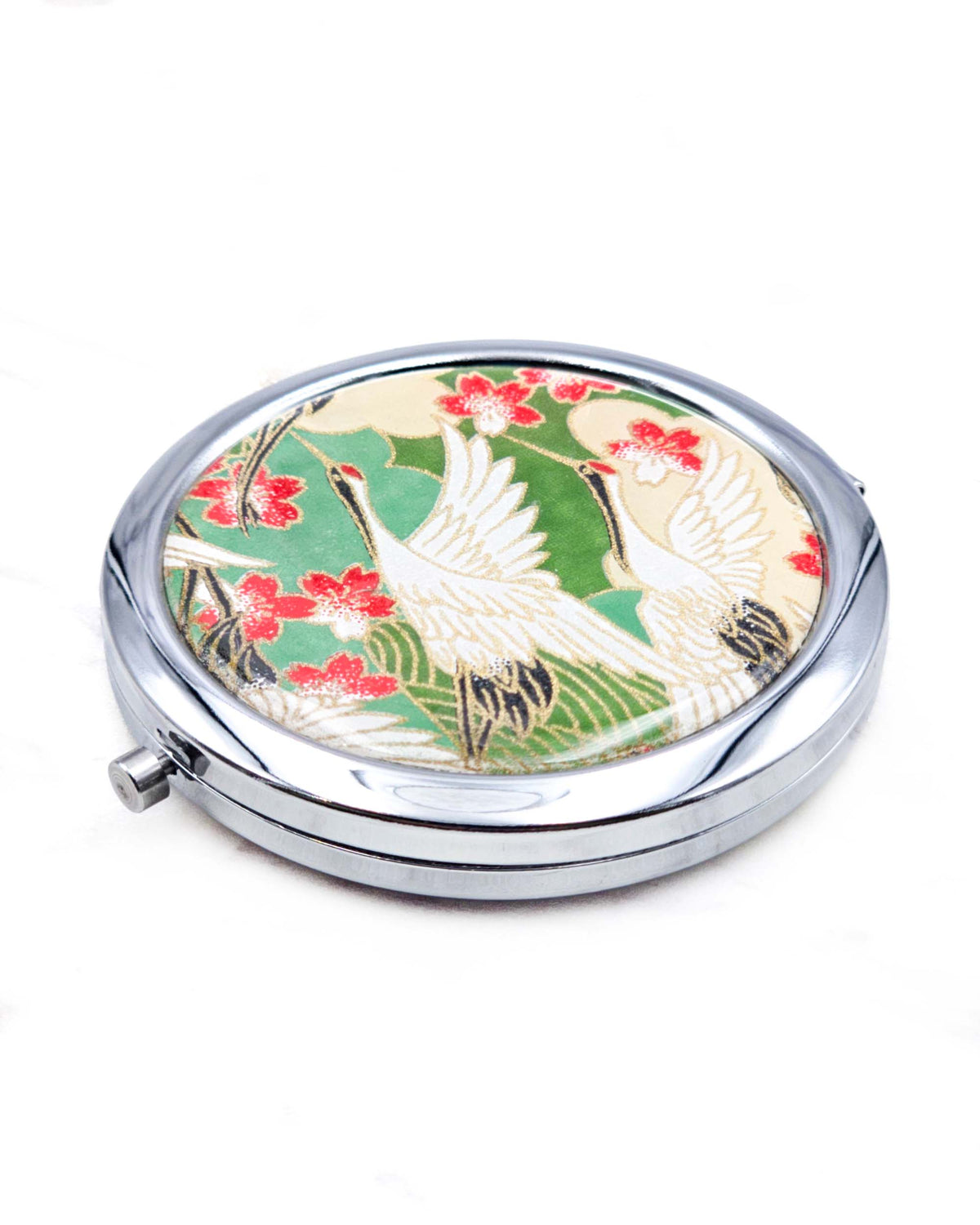 Round silver metal compact mirror featuring white flying cranes and red and white cherry blossoms on a green background with metallic gold details.