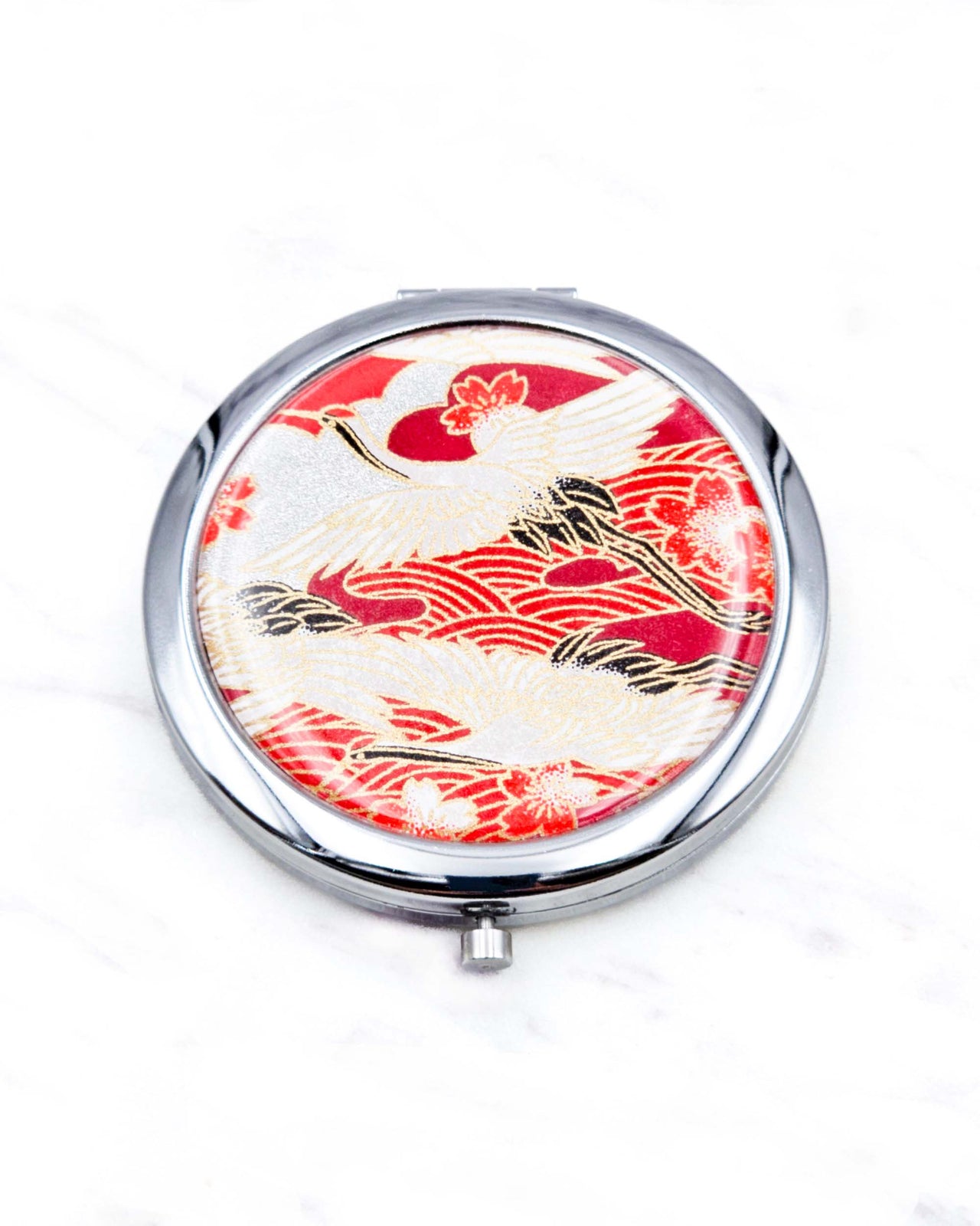 Round silver metal compact mirror featuring white flying cranes and red and white cherry blossoms on a red background with metallic gold details.