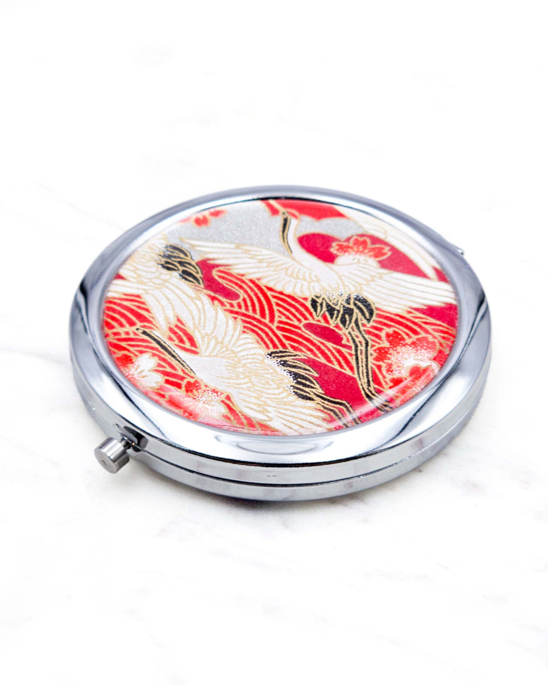 Round silver metal compact mirror featuring white flying cranes and red and white cherry blossoms on a red background with metallic gold details.