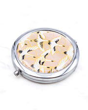 Round silver metal compact mirror featuring white flying cranes on a light pink background with metallic gold accents.