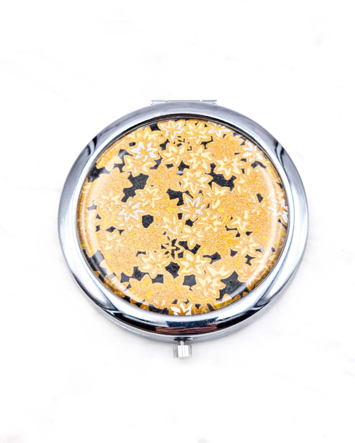 Round silver metal compact mirror featuring small gold and white momiji (maple leaves) on a black background with metallic gold details.