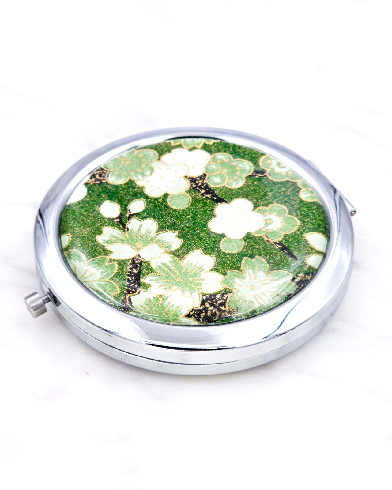 Silver metal compact mirror featuring green cherry blossoms on a green background with metallic gold accents.