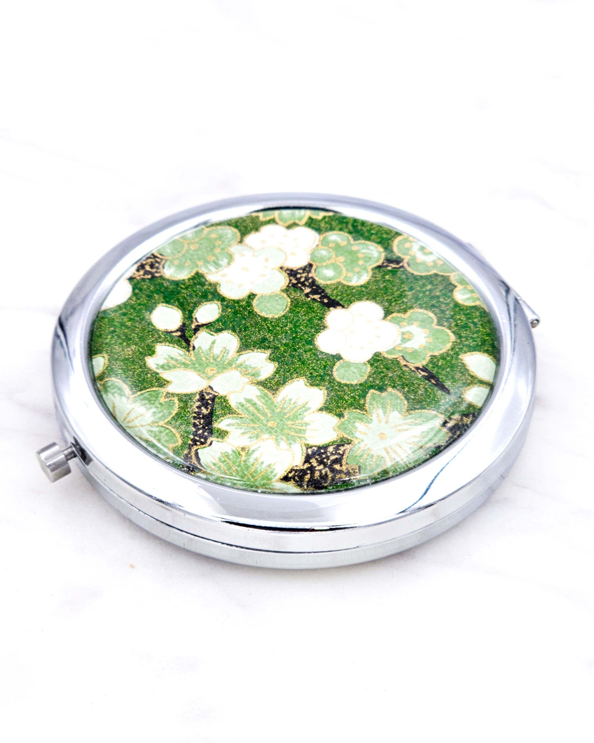 Silver metal compact mirror featuring green cherry blossoms on a green background with metallic gold accents.