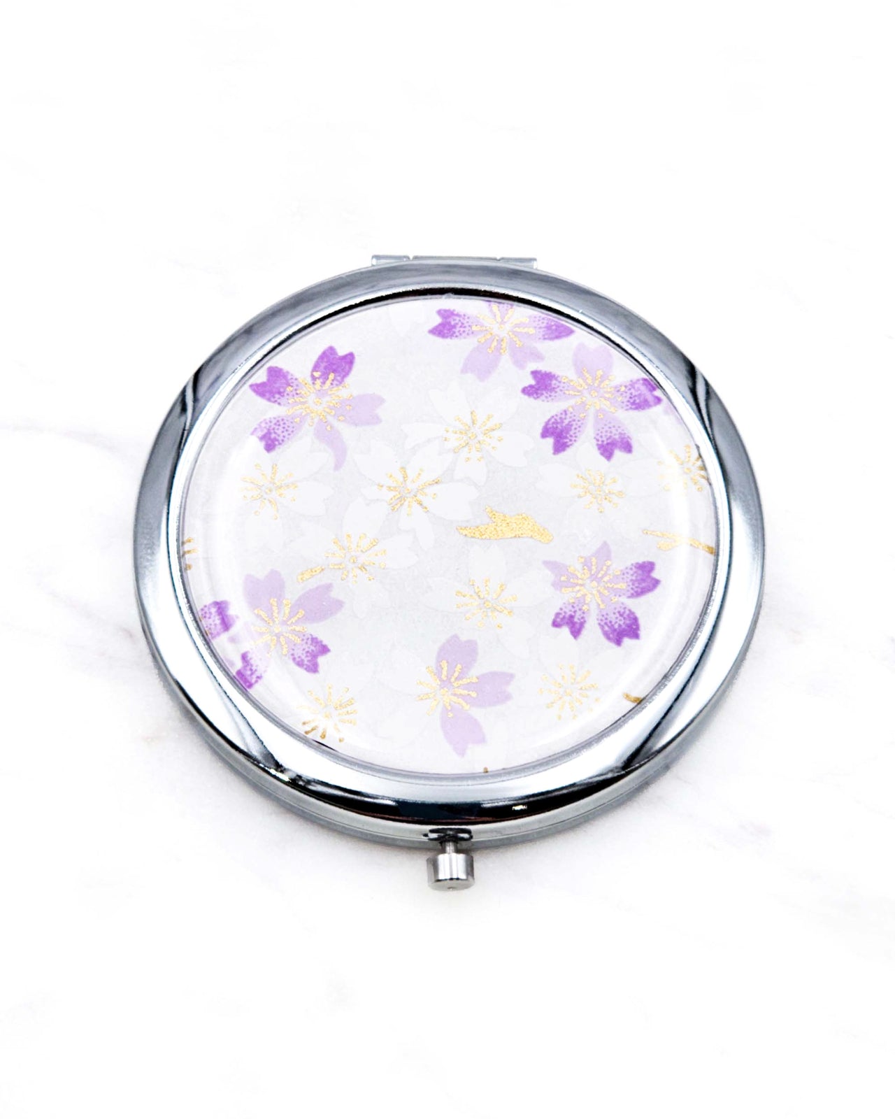 Round silver metal compact mirror featuring light purple and white cherry blossoms on a white background with metallic gold accents.
