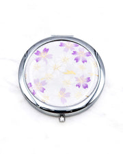 Round silver metal compact mirror featuring light purple and white cherry blossoms on a white background with metallic gold accents.