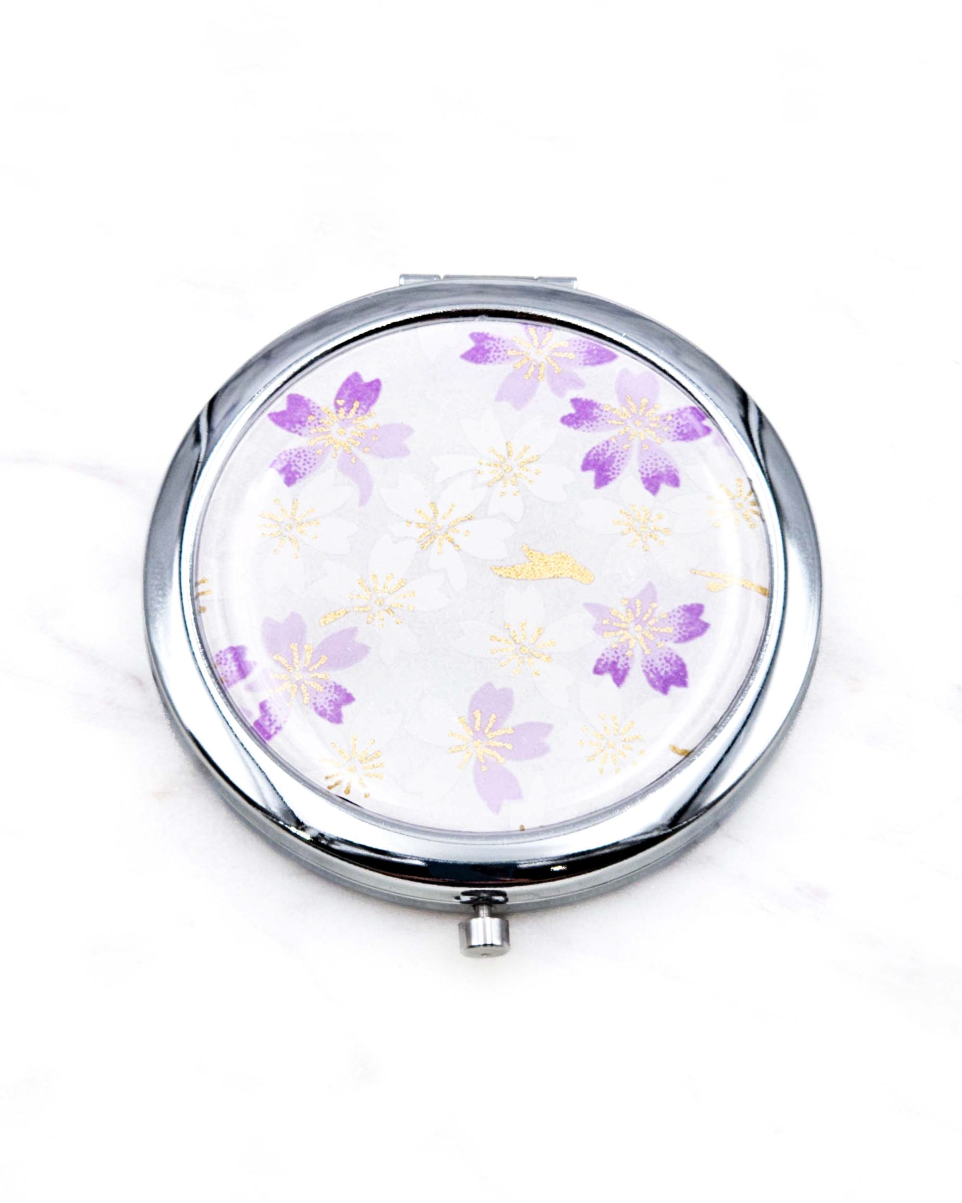 Round silver metal compact mirror featuring light purple and white cherry blossoms on a white background with metallic gold accents.