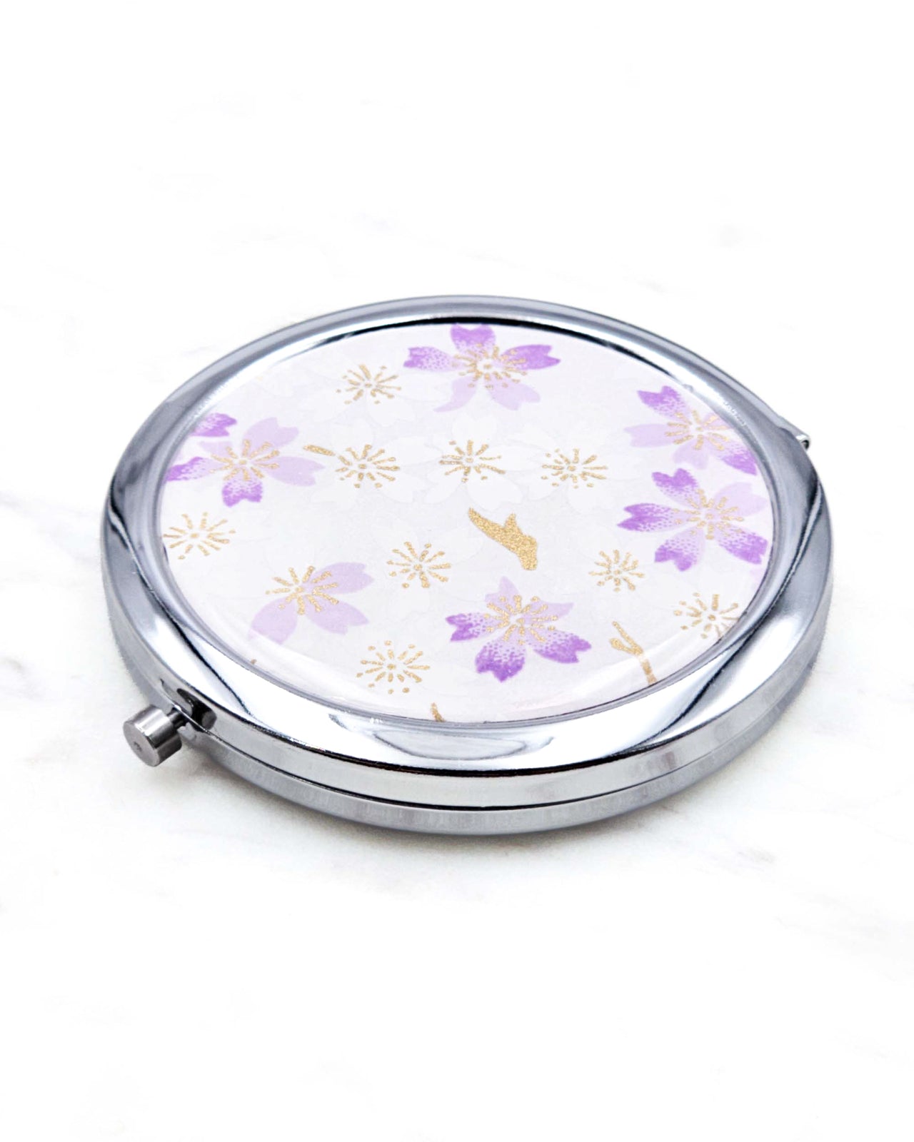 Round silver metal compact mirror featuring light purple and white cherry blossoms on a white background with metallic gold accents.