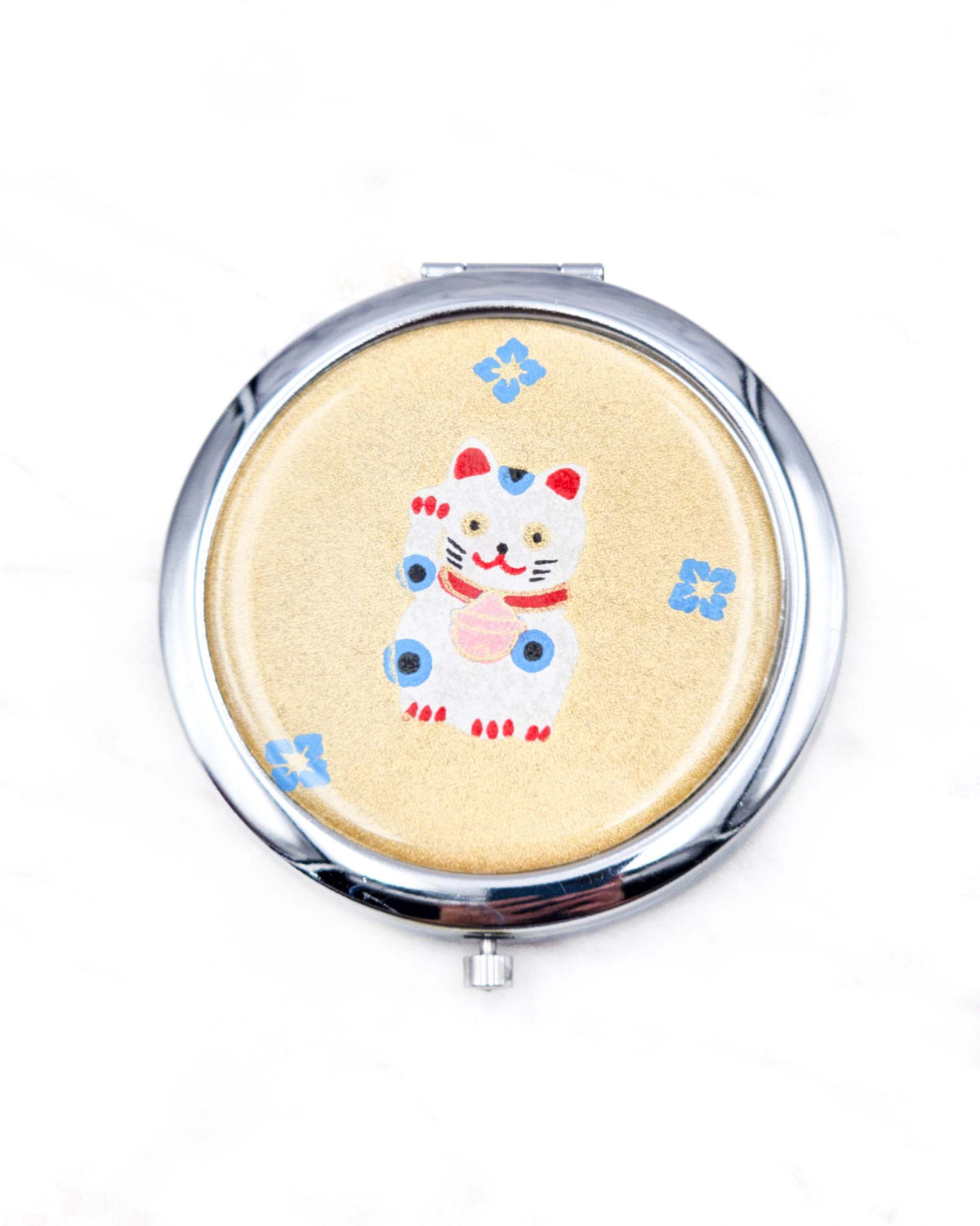 Round silver metal compact mirror featuring a white, red, and blue maneki-neko (lucky cat) with blue hanabishi (flower diamond) motifs on a metallic gold background.