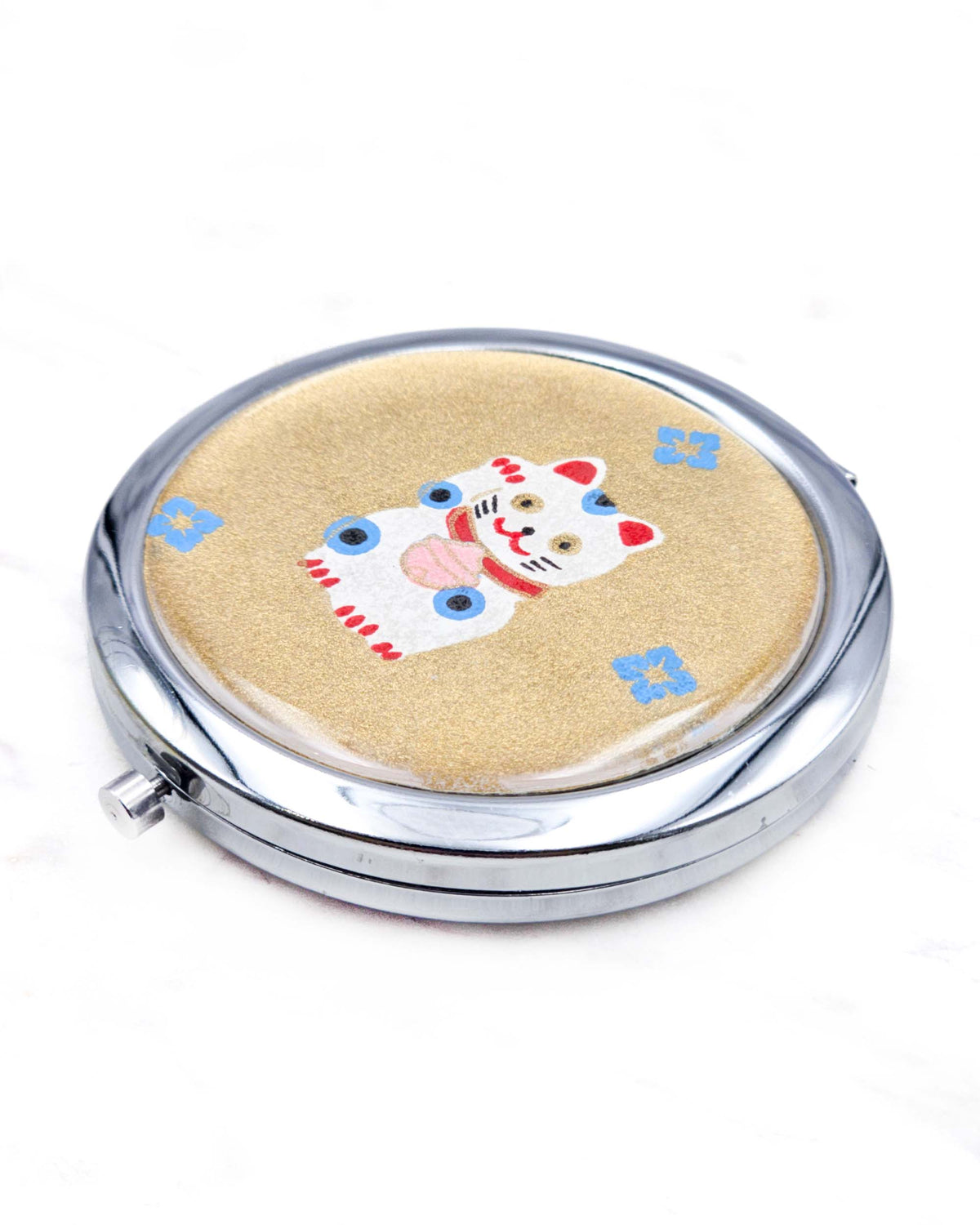 Round silver metal compact mirror featuring a white, red, and blue maneki-neko (lucky cat) with blue hanabishi (flower diamond) motifs on a metallic gold background.