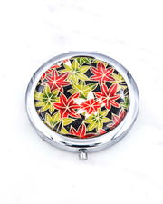 Silver metal compact mirror featuring green, red, and white maples leaves on a black background with metallic gold accents.