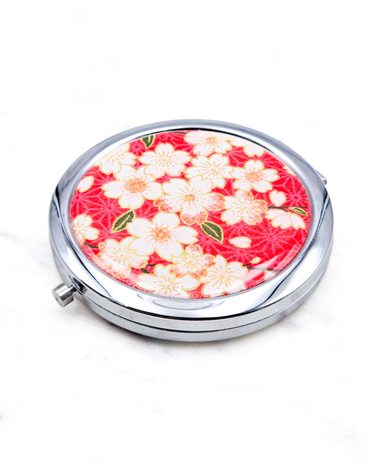 Round silver metal compact mirror featuring pink and white cherry blossoms on a red asanoha (hemp leaf) patterned background with metallic gold details.