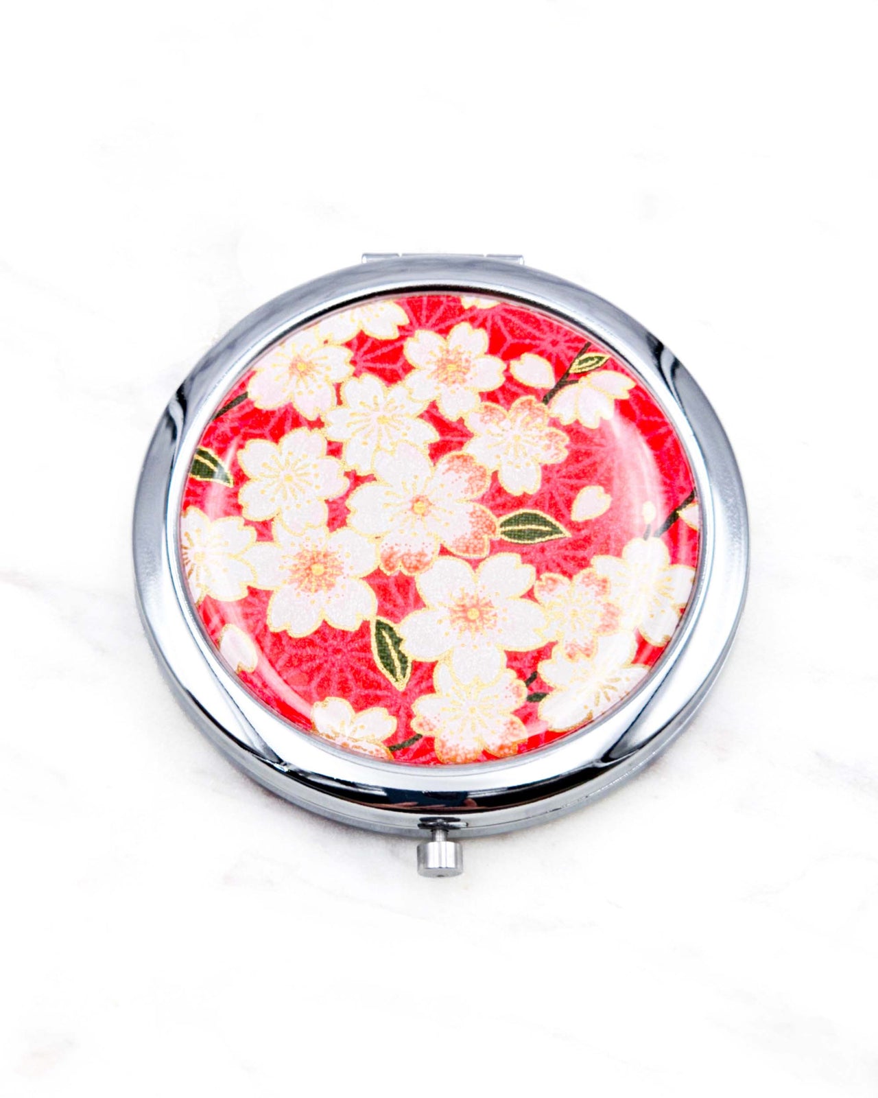 Round silver metal compact mirror featuring pink and white cherry blossoms on a red asanoha (hemp leaf) patterned background with metallic gold details.