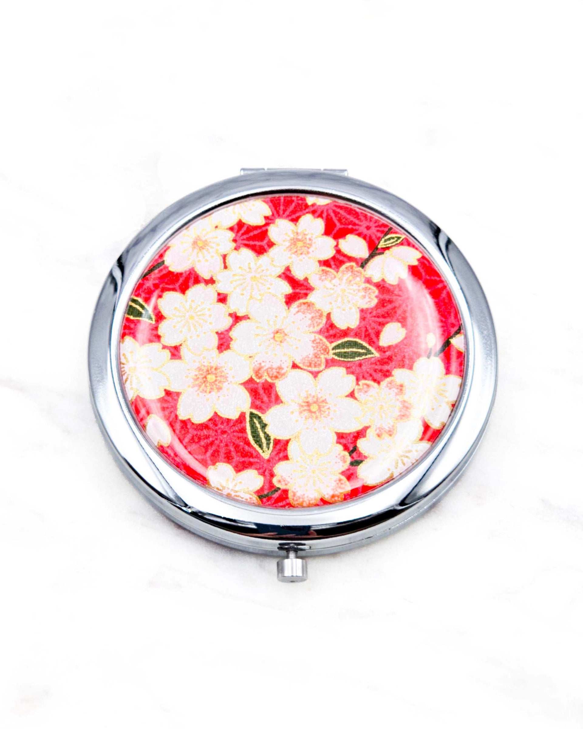 Round silver metal compact mirror featuring pink and white cherry blossoms on a red asanoha (hemp leaf) patterned background with metallic gold details.