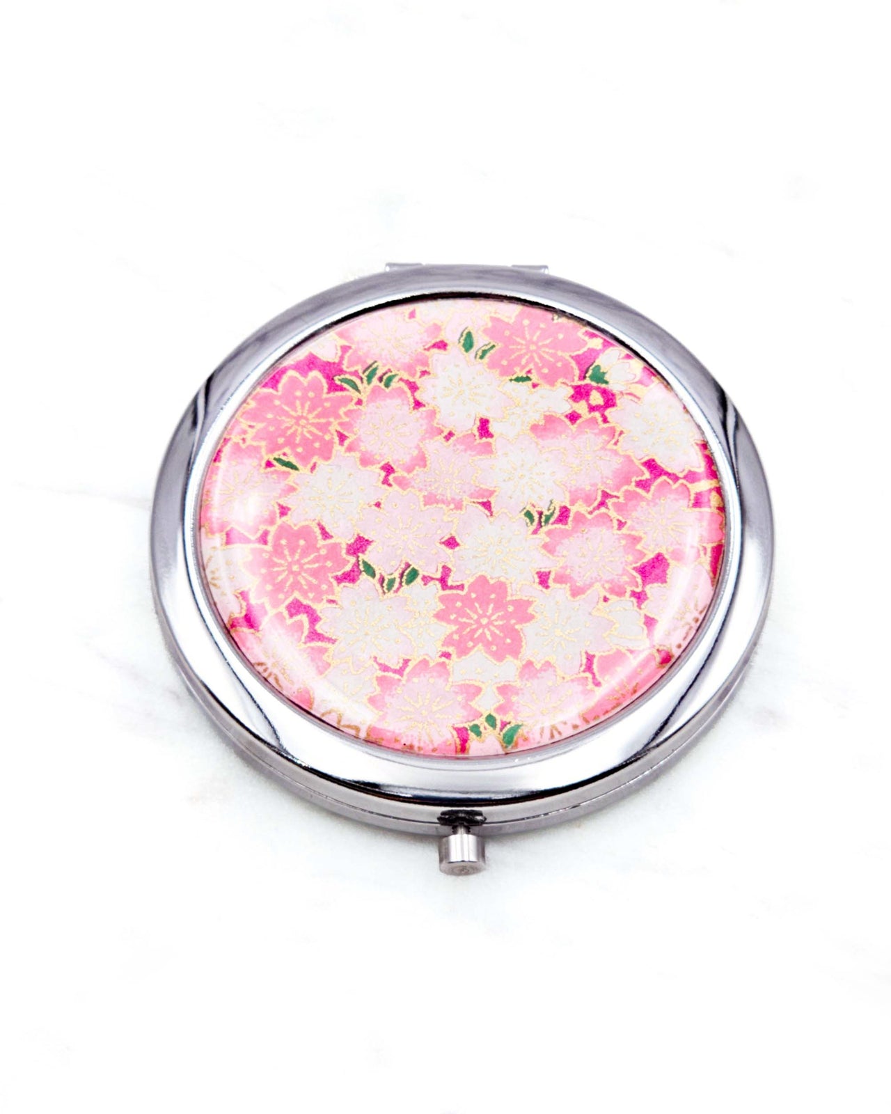 Round silver metal compact mirror featuring pink and white cherry blossoms on a magenta pink background with metallic gold accents.