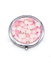 Round silver metal compact mirror featuring pink and white cherry blossoms on a magenta pink background with metallic gold accents.