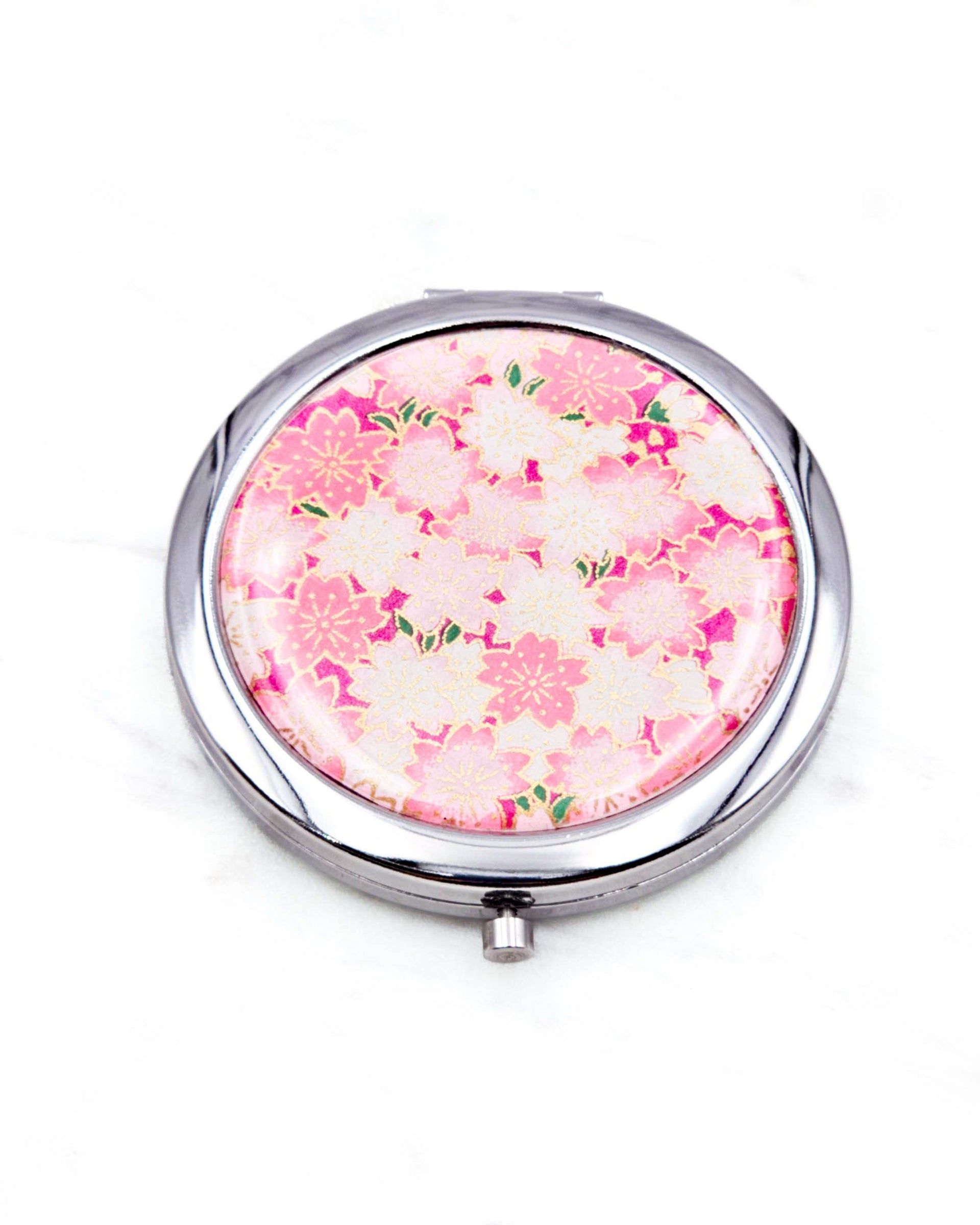 Round silver metal compact mirror featuring pink and white cherry blossoms on a magenta pink background with metallic gold accents.