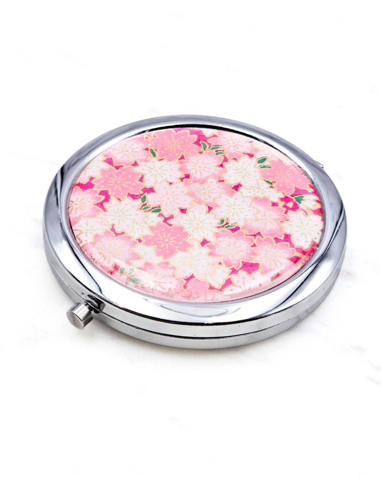 Round silver metal compact mirror featuring pink and white cherry blossoms on a magenta pink background with metallic gold accents.