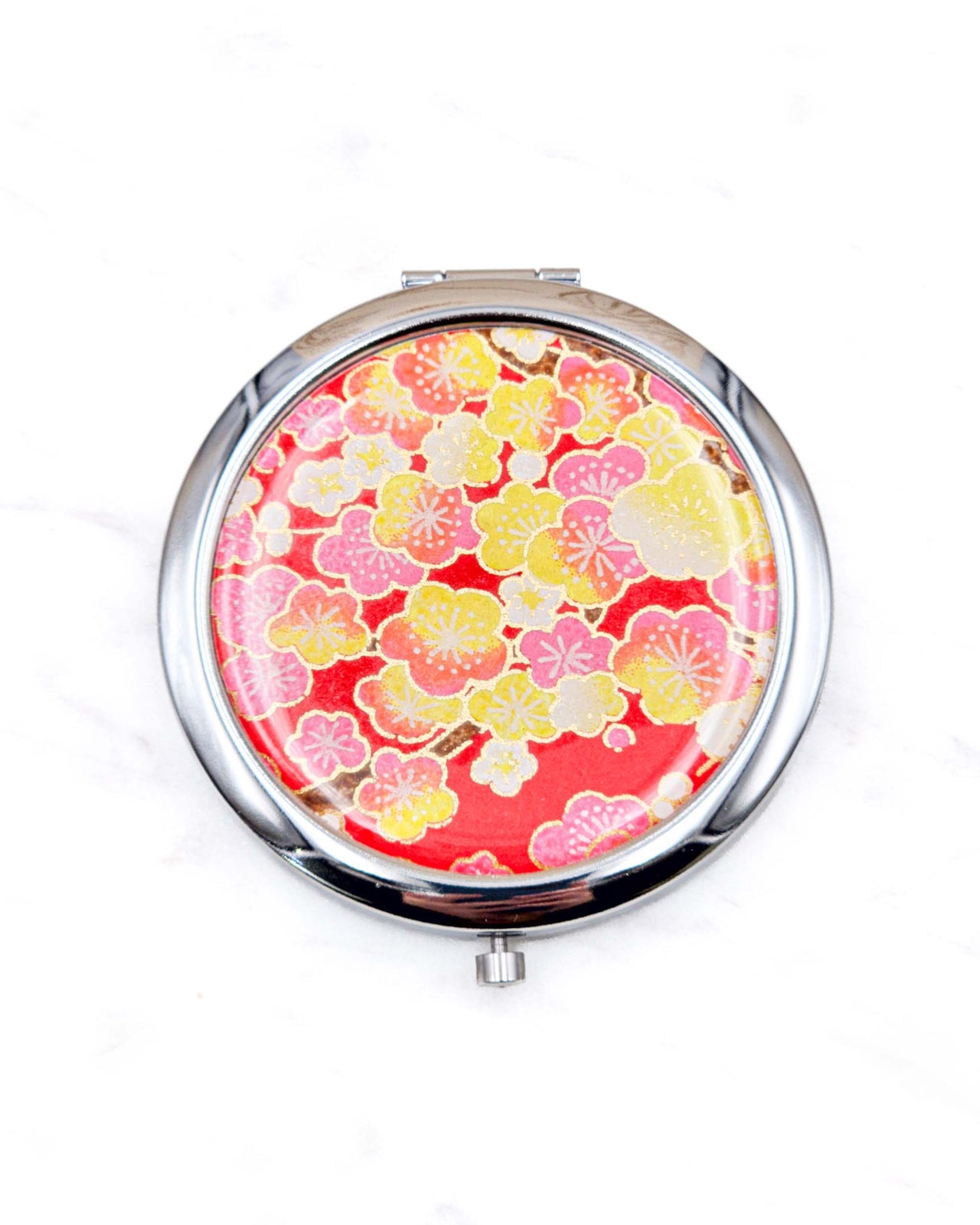 Round silver metal compact mirror featuring pink, yellow, and white plum blossoms on a red background with metallic gold details.