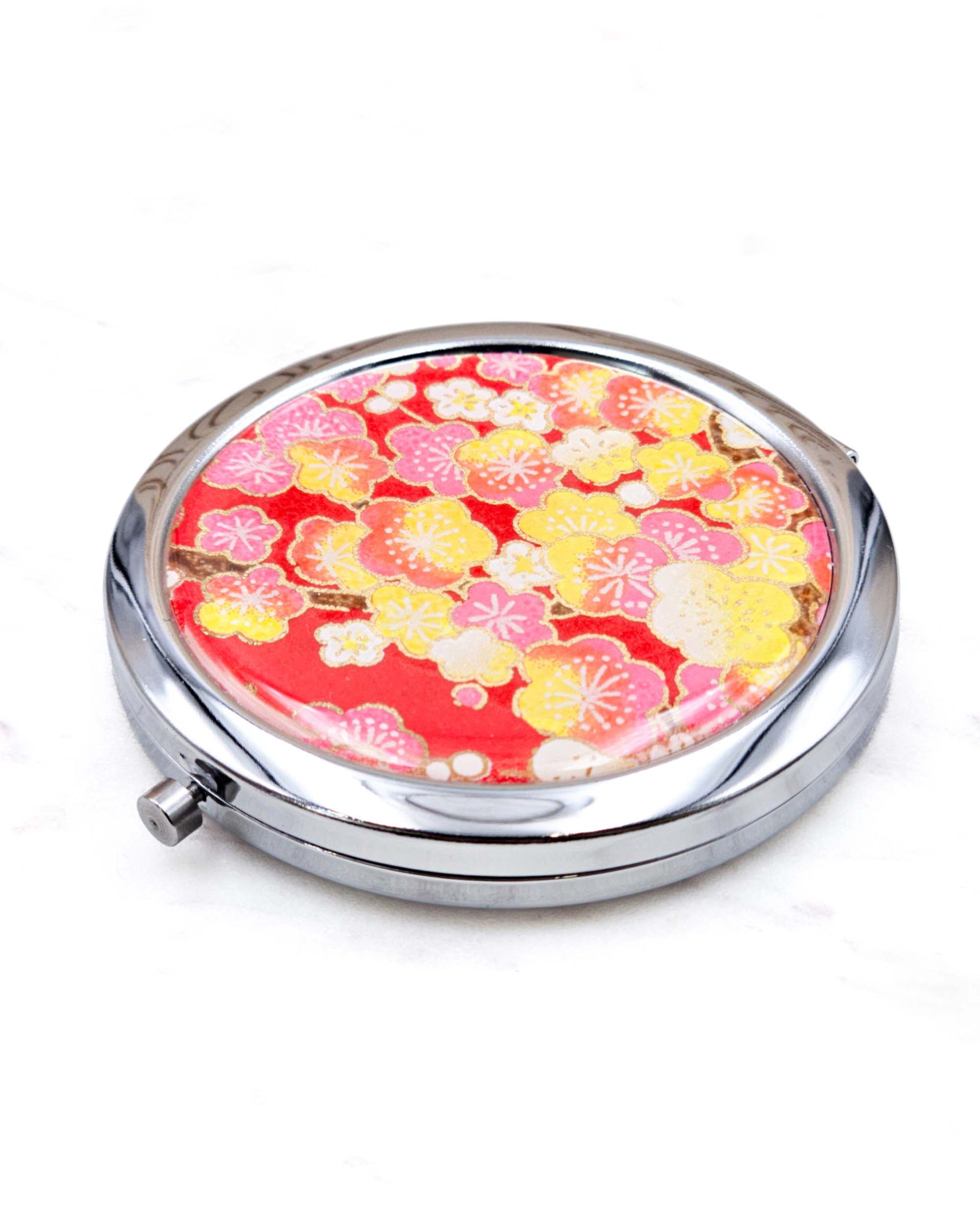 Round silver metal compact mirror featuring pink, yellow, and white plum blossoms on a red background with metallic gold details.