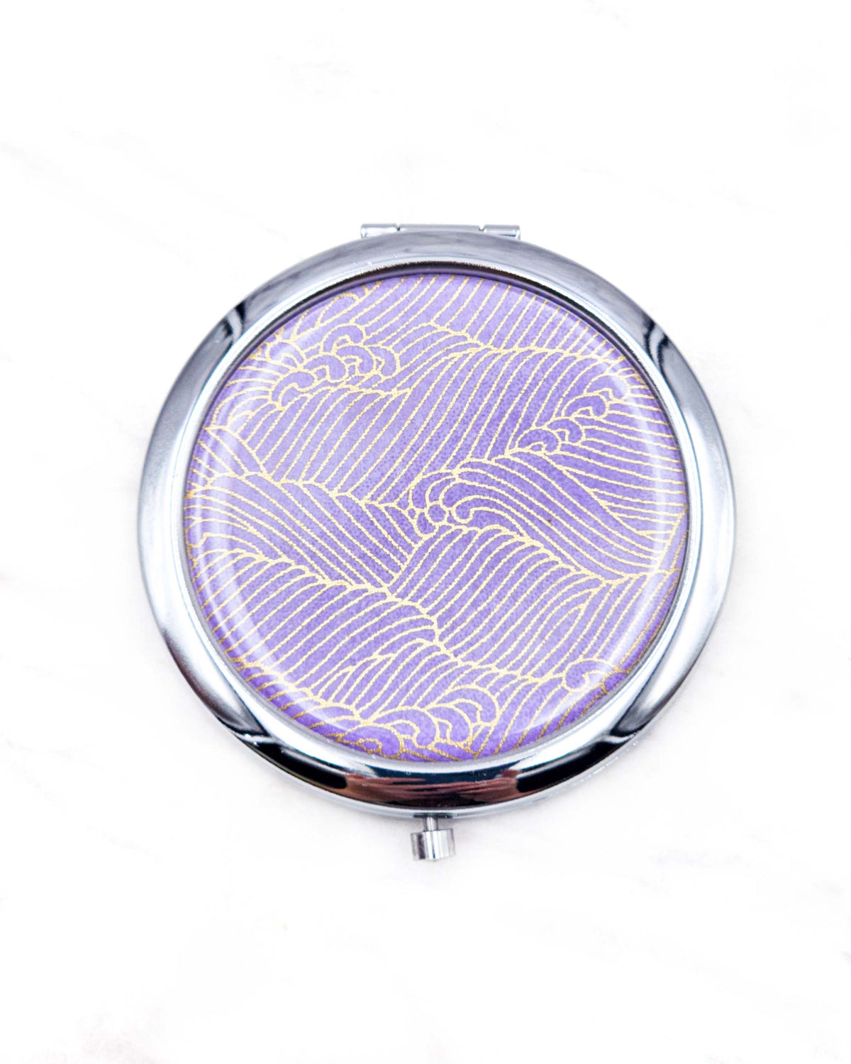 Round silver metal compact mirror featuring small metallic gold waves (aranami) on a gradient purple background.