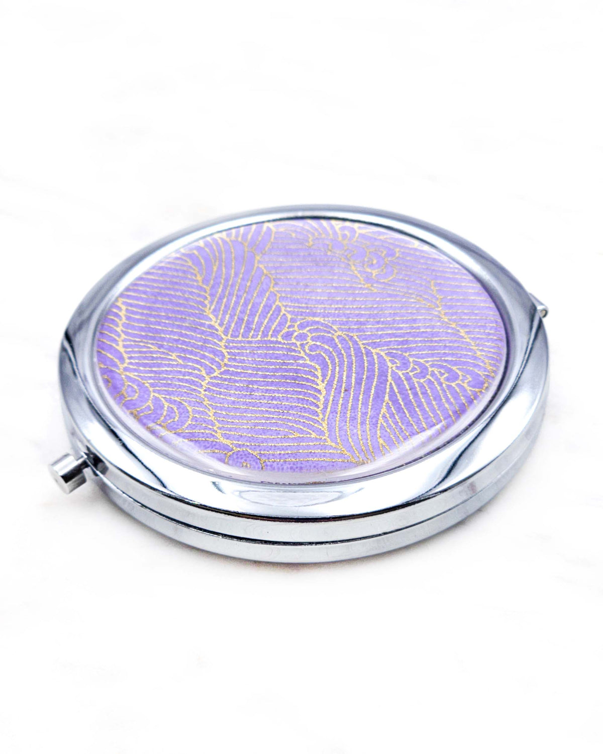 Round silver metal compact mirror featuring small metallic gold waves (aranami) on a gradient purple background.