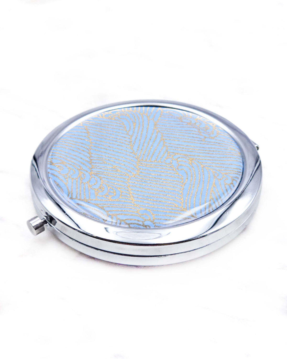 Round silver metal compact mirror featuring small metallic gold waves (aranami) on a light blue background.