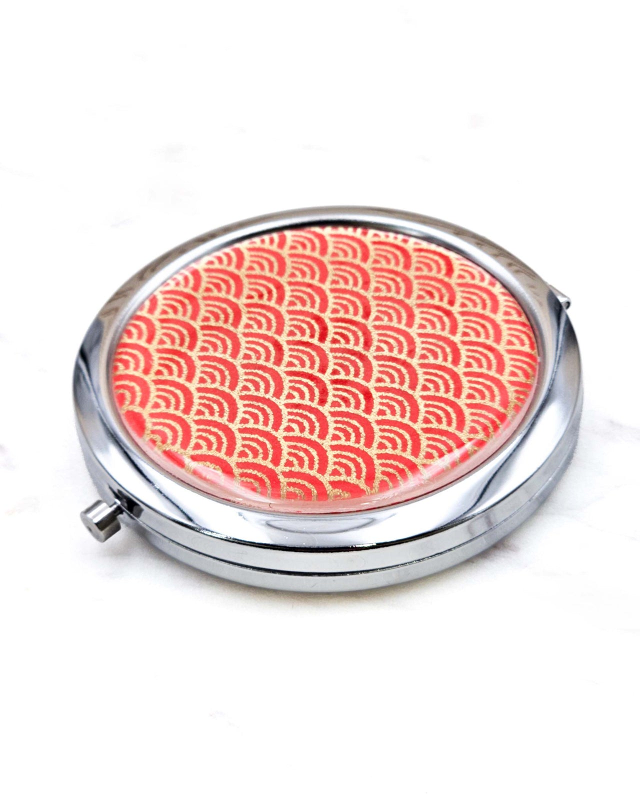 Round silver metal compact mirror featuring a small traditional red and metallic gold seigaiha (wave crests) pattern.